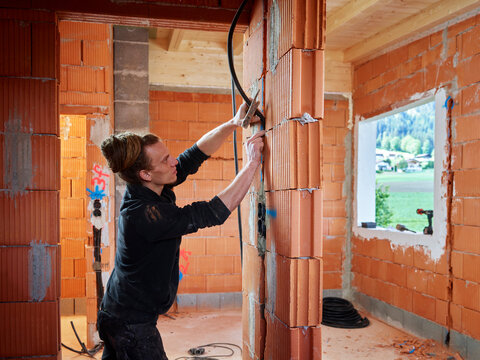 Male electrician installing cables between bricks while working at construction site