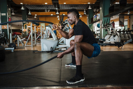 Muscular sportsman exercising with rope during sports training in gym