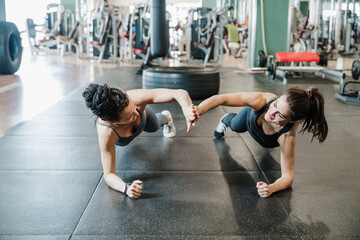 Female athlete friends giving high-five while doing plank in health studio