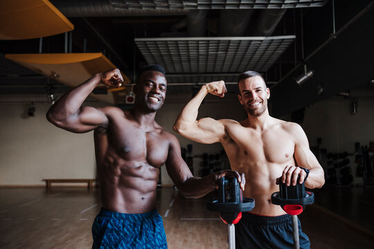 Handsome shirtless male athletes flexing muscles while standing in health club