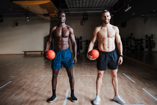 Confident male athletes holding sports ball while standing in health studio