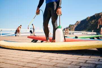unrecognizable surf instructor in neoprene disinfecting surfboards on the beach
