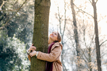 Smiling mid adult woman looking while embracing tree at park
