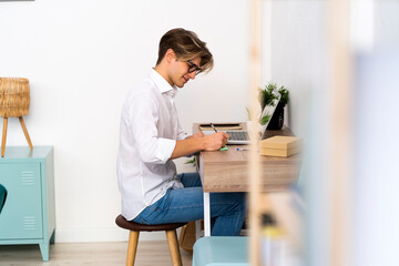 Young man writing while sitting at table in living room