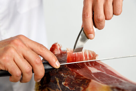 Hands of male butcher cutting Iberian ham at shop
