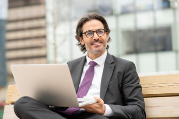 Smiling male entrepreneur with laptop looking away while sitting on bench