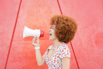 Redhead woman shouting on megaphone by red wall