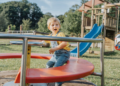 Charming boy sitting on merry go round in playground