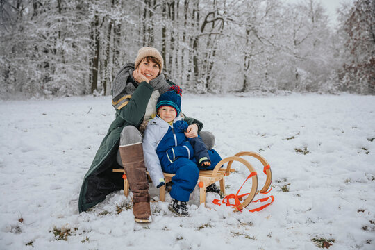 Mother and son sitting on sled at snowy field during winter