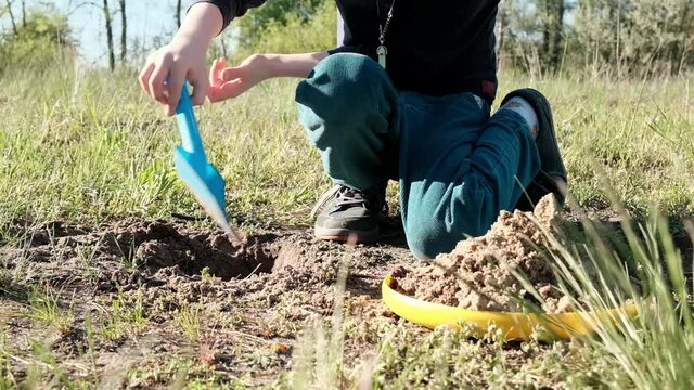 A young boy is digging a hole in the ground with a toy shovel.