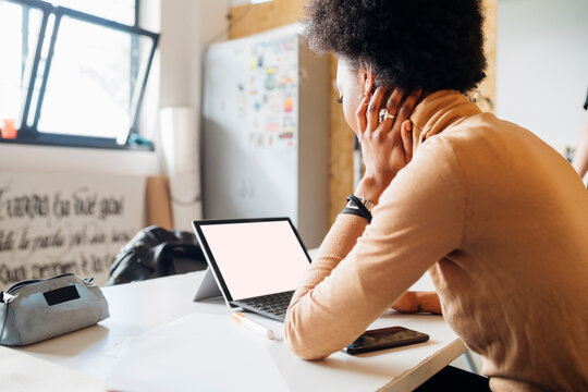 Young African woman using laptop while sitting at table in studio
