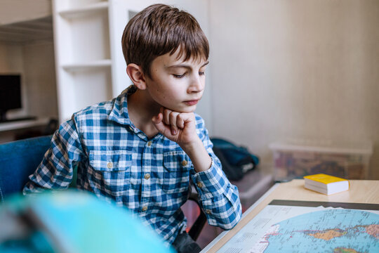 Boy with hand on chin studying map at table