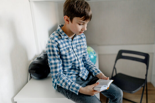 Boy reading dictionary while sitting on table at home