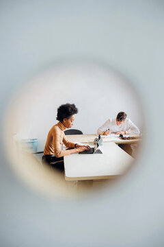 Young multi ethnic couple seen through hole working at studio