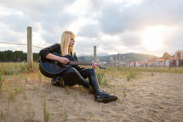 Female musician playing guitar while sitting on sand