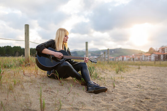 Female Musician Playing Guitar While Sitting On Sand