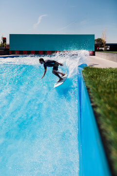 Mid adult athlete surfing on surfboard over swimming pool wave