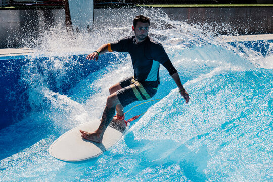 Athlete with surfboard surfing on swimming pool wave