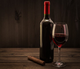 Bottle of red wine with a glass of red wine and cuban cigar on an old wooden table