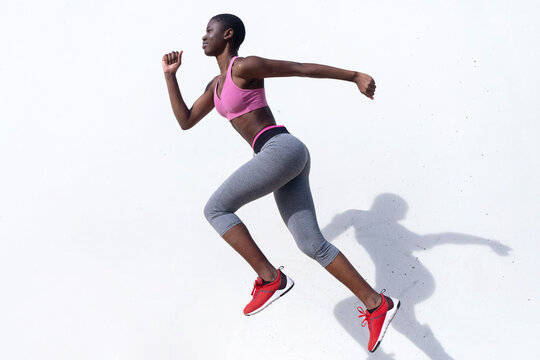 Female runner jumping while practicing against white wall