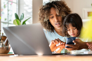 Mother multi-tasking while working on smart phone with daughter in home office