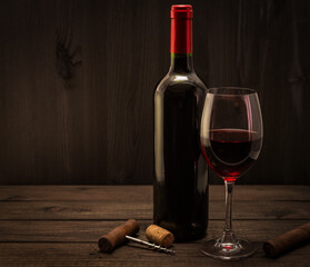 Bottle of red wine with a glass, corkscrew and cuban cigar on an old wooden table