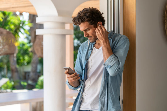 Man Using Smart Phone While Listening Music Through Headphones At Doorframe