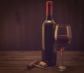 Bottle of red wine with a glass and corkscrew with cork on an old wooden table