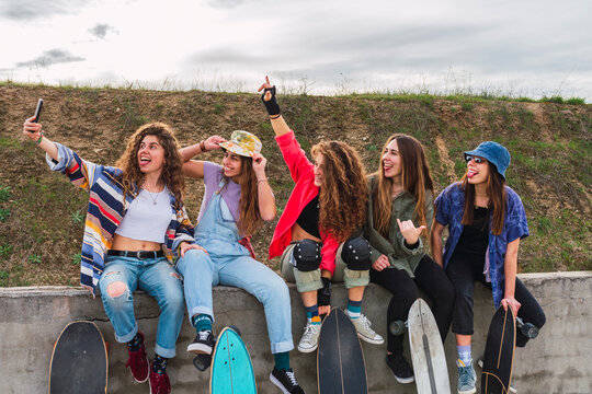 Happy female friends taking selfie through mobile phone on retaining wall