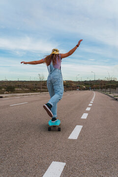 Woman in bib overall skating with skateboard on road