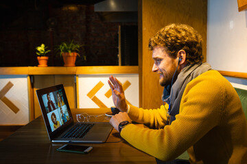 Male owner waving during video call on laptop while sitting at cafe
