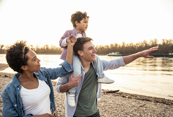 Young man carrying boy on shoulders while standing by woman at lakeside