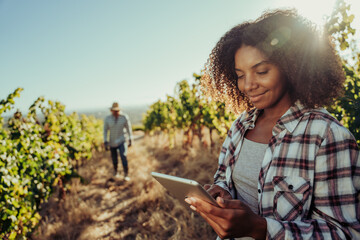 Mixed race female farmer smiling working in vineyards researching about vines on digital tablet...