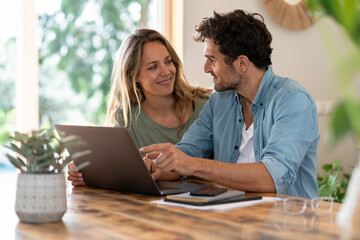 Smiling couple looking at each other while sitting in front of laptop at table