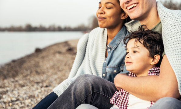 Cute boy sitting with parents covered in blanket during sunset