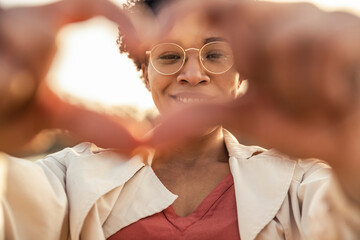 Smiling woman gesturing heart shape with hand outdoors