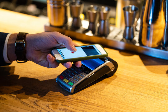 Man doing contactless payment with smart phone through credit card reader at cafe