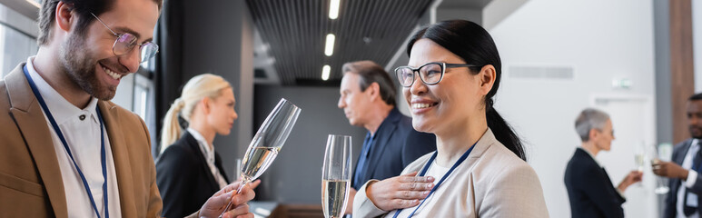 asian businesswoman talking to young businessman near blurred colleagues, banner
