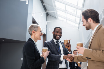 happy african american businessman shaking hands with young colleague during coffee break - obrazy, fototapety, plakaty