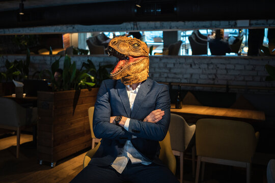 Businessman wearing dinosaur mask while sitting with arms crossed in cafe