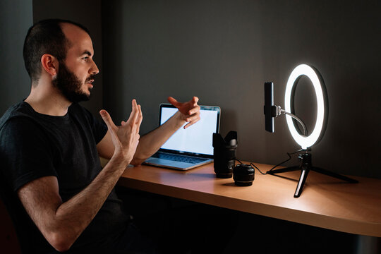 Mid adult influencer vlogging over mobile phone attached with illuminated circular strobe at studio