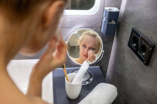 Woman using cotton pad while looking in mirror at bathroom