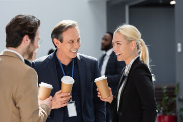 smiling businesspeople talking and holding paper cup during coffee break