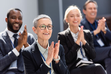 Fototapeta premium selective focus of mature businesswoman applauding during seminar near interracial colleagues