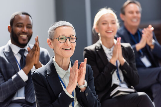 selective focus of mature businesswoman applauding during seminar near interracial colleagues