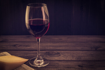 Glass of red wine with a piece of parmesan on an old wooden table. Focus on the stem glass