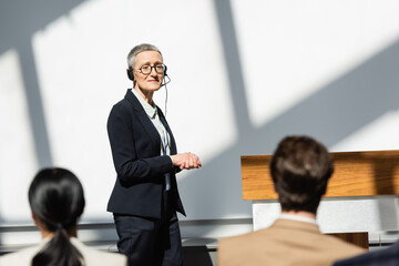 mature lecturer in headset looking at participants on blurred foreground