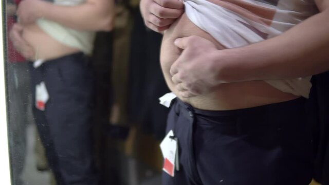 A man with tries on pants in a dressing room of a store and touches a big belly