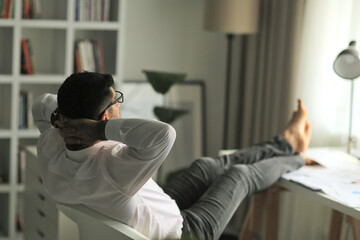 businessman leaning back in his chair with his feet on a desk and hands behind his head.