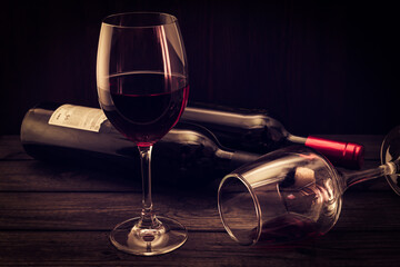 Two bottles of red wine with two glasses on an old wooden table. Focus on an overturned glass of wine